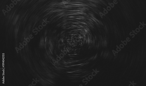 Abstract dark circular motion texture with radial blur effect. Black grunge background featuring subtle light streaks forming a vortex pattern, creating a dynamic and dramatic backdrop with centered c