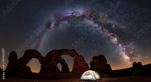 Milky Way galaxy arching over red sandstone rock formations with a glowing camping tent silhouette in the desert at night.
