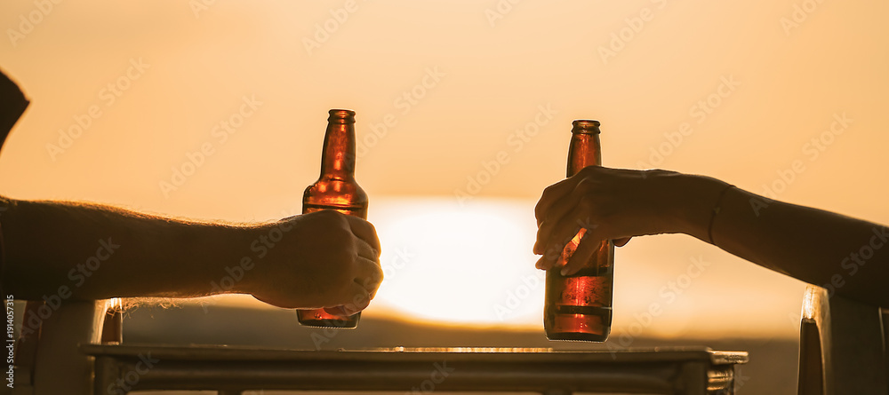 Naklejka premium beer bottles in the hands of vacationers, which are held by a couple of lovers or friends. Camping together on the beach and a trip to a warm country for a honeymoon