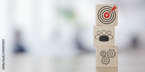 Stack of wooden blocks with team, process and goal or target icons on table in front of office background with selective focus and copy space, business process or achievement concept