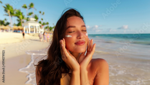 Tableau sur toile Woman applying sunblock on her face while relaxing on sandy beach during her sum