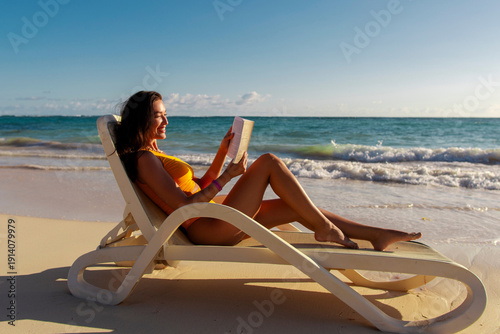 Obraz na płótnie Lady lying on sun lounger chair on the beach and reading book, enjoying perfect