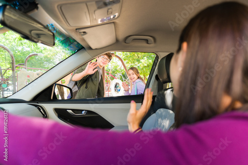 Mother waving goodbye to her teen children at school drop off, parent driving kids to campus
