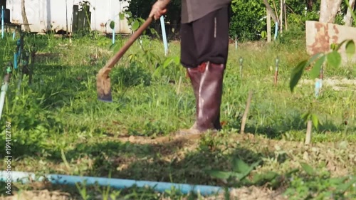 Happy gardener man farmer working agriculture field removing weed green grass with hoe wearing boot rural farmland outdoor clearing grassy soil warm