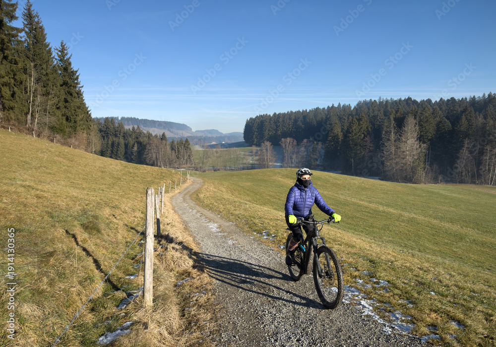 Fototapeta premium Woman cycling with her electric mountain bike on a cold and icy winterday in t5he Allgaeu Alps, Bavaria, Germany 