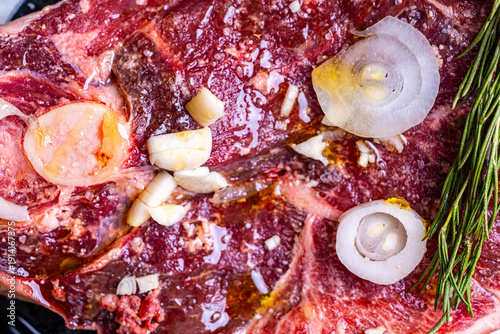 Raw lamb meat on a baking sheet with onions, rosemary, garlic, cut into steaks is ready for frying. The process of cooking lamb.