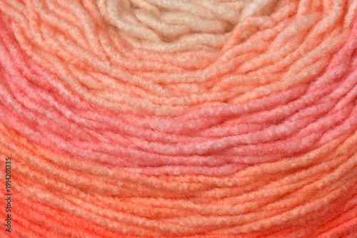 Macro close up shot of a soft yarn ball with a smooth color gradient from peach to pink and orange in a circular pattern
