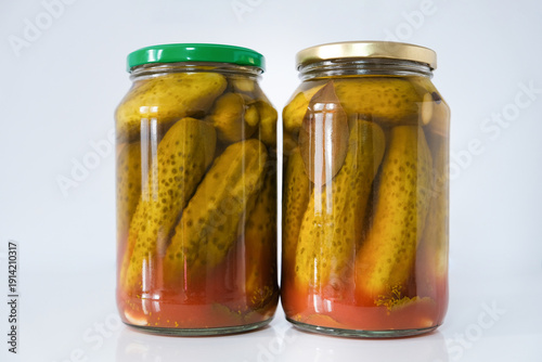 Glass jars with salted pickled cucumbers in tomato sauce, homemade preservation on a light background