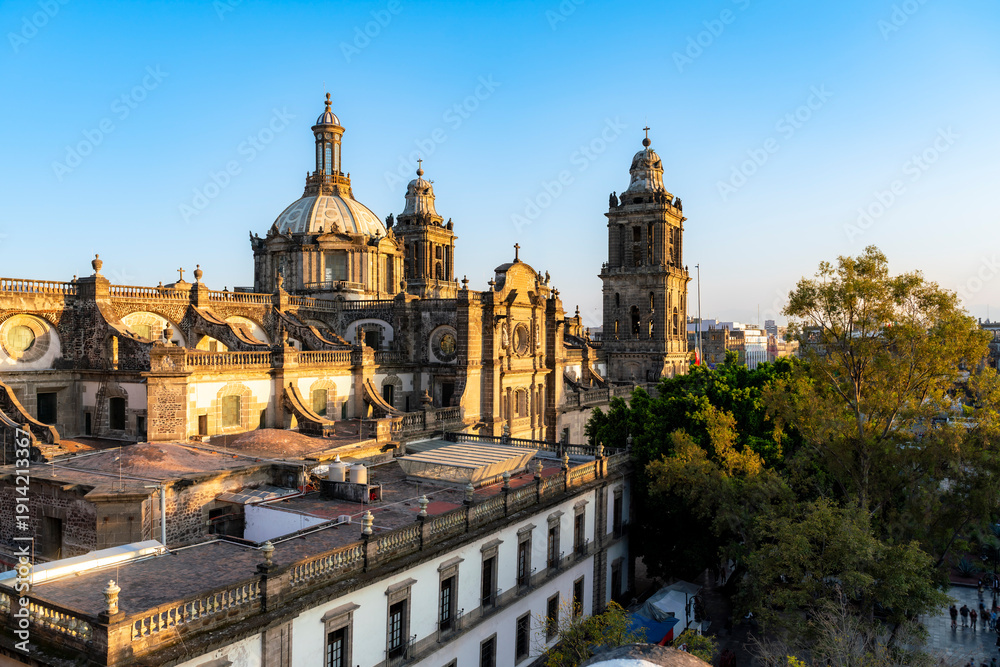Fototapeta premium Late afternoon sunlight illuminates the iconic Metropolitan Cathedral and Zocalo in Mexico City. The colonial architecture glows with golden under a clear sky, highlighting the city's historical urban