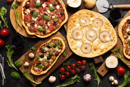 Several pizzas on a dark table. Meat pizza, pear pizza, and mushroom pizza