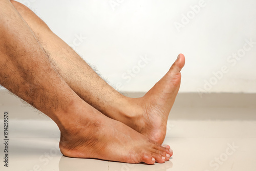 Fotografi Man's hairy legs and feet resting on a white floor, isolated against a white background