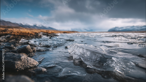 Wallpaper Mural Ice fragments on a rocky shoreline beside a calm river, with distant mountains and cloudy skies, for themes about climate change and global warming, glacial melt and rising sea levels Torontodigital.ca