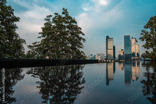 city skyline with skyscrapers reflected in calm water of lake or swimming pool at sunset, Modern cityscape of Bangkok with highrise towers mirrored on tranquil waterfront under evening sky