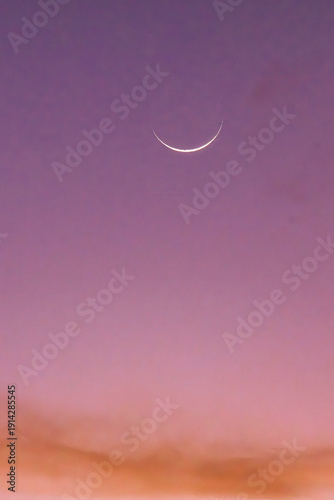 Sliver moon in a pink sky at sunset.