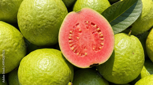 A vibrant pink guava cut open revealing its juicy pulp surrounded by green guavas