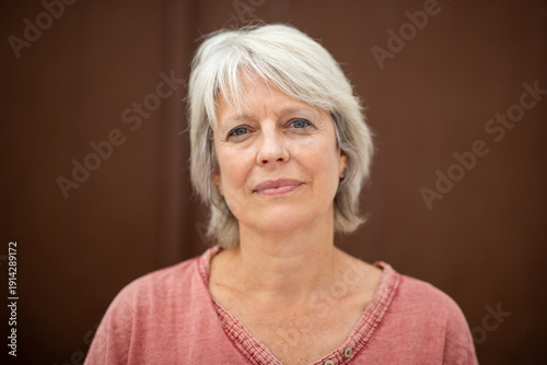 Foto Serious mature woman with white hair against brown wall