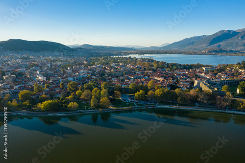 Bild auf Leinwand Aerial perspective reveals the city of Ioannina bordered by Lake Ioannina, with red-tiled rooftops, lush trees, and the Pindus mountains rising in the background