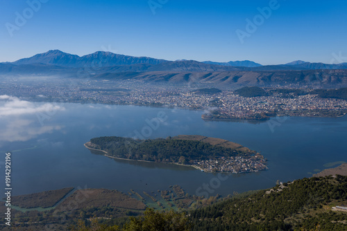 Foto Expansive elevated view of the tree-covered Island of Ioannina set in tranquil lake waters, with the city of Ioannina and the Pindus mountains forming a dramatic backdrop