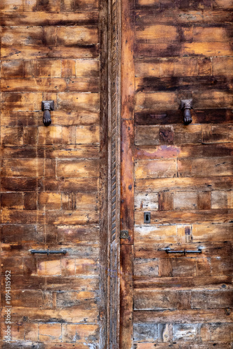 Close up of an ancient weathered wooden door with traditional iron hand knockers and rustic texture in the historic town of Siguenza Spain featuring medieval craftsmanship and antique details