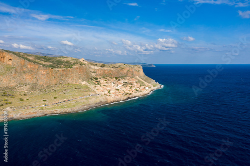 Fotografie Aerial view of the historic Monemvasia village nestled beneath steep orange cliffs along the vivid blue Mediterranean Sea