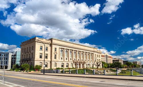 Des Moines Historic City Hall in Iowa. Historic Beaux-Arts architecture features a limestone facade with columns and arched windows near the river under a blue sky