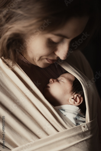 Woman holding sleeping baby in elastic baby wrap in bright color, indoor shot