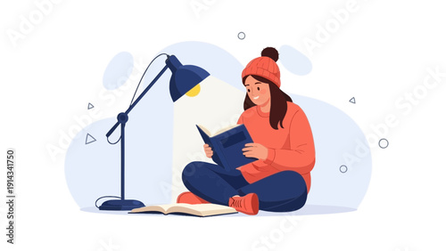 Young woman in warm clothes reading a book under a desk lamp