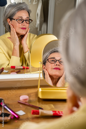 Foto Senior woman applying moisturizer, touching her face and looking at reflection i