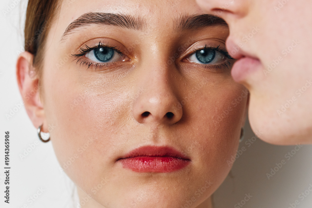 Fototapeta premium Close up portrait of young woman with blue eyes and red lips looking at camera with serious expression against white background. Beauty, skin, face details.