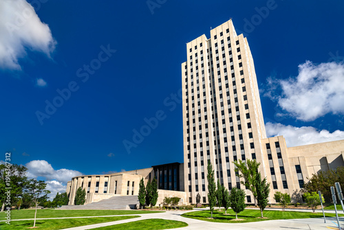 North Dakota State Capitol in Bismarck. Historic Art Deco skyscraper features a limestone facade and legislative wing on green grounds under a blue sky