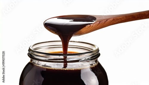 Dark Viscous Liquid Pouring From A Wooden Spoon Into A Glass Jar