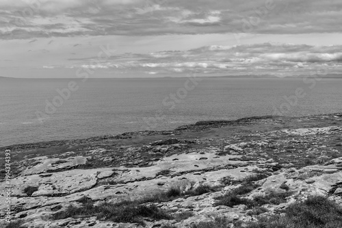 A black and white photo of a rocky shoreline with a calm ocean in the background