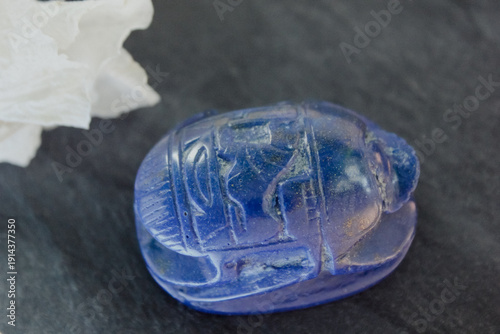 Photos Lapis lazuli scarab figurine on dark stone with white petals, ancient Egyptian protection symbol