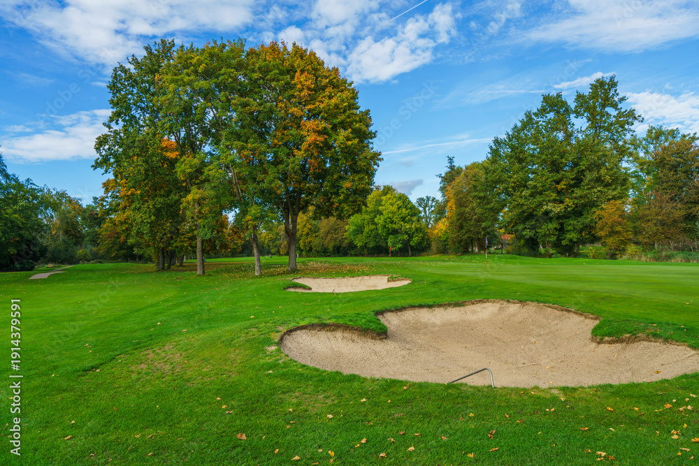 Fototapeta premium a professional golf course fairway featuring well-maintained sand traps and lush green grass. Beautiful autumn foliage on surrounding trees creates a peaceful outdoor sports atmosphere