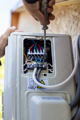Installing the air conditioner external unit. A worker uses a screwdriver to connect the air conditioning system electrical control cable