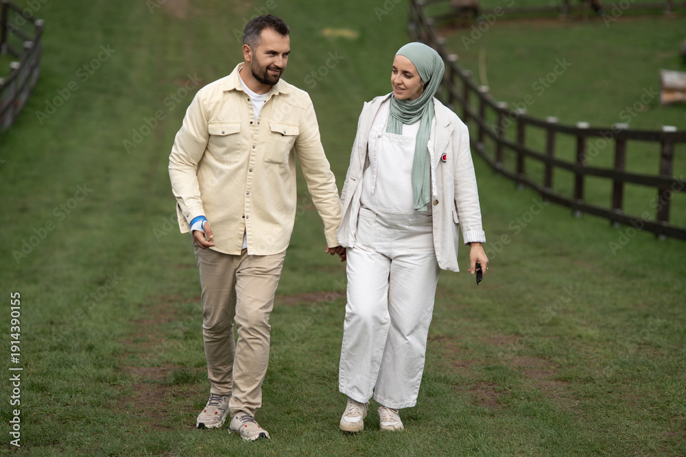 Fototapeta premium A happy couple holding hands in a lush green park, enjoying a romantic moment together, a pregnant woman in hijab, and a man with a broken arm, outdoor love story, connection, happiness, nature.