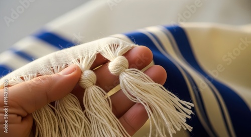 Hand holding fringes of Jewish prayer shawl, showing traditional blue stripes on soft fabric. Sacred Jewish prayer shawl with carefully tied tzitzit knots and white tassels.
