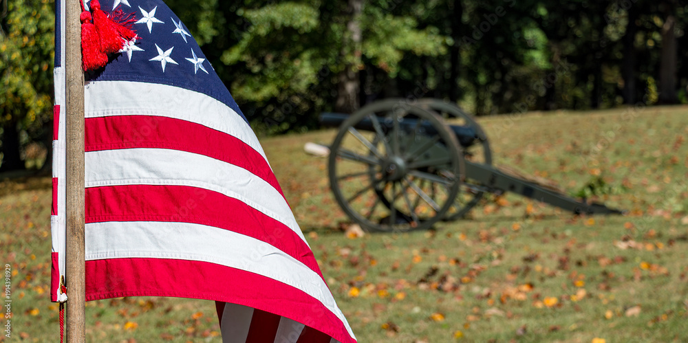 Fototapeta premium The American flag at a Civil War reenactment with an out-of-focus Civil War era cannon in the background. There is copy space in the image.