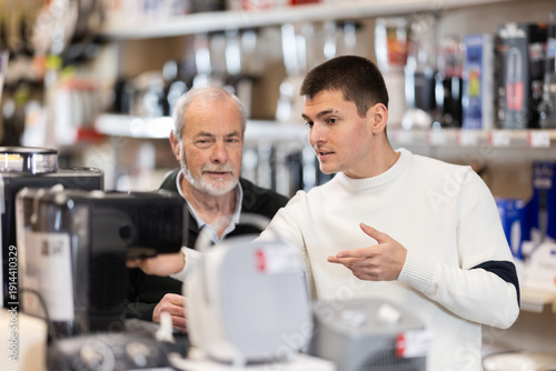Fotografie Senior man with help of guy sales consultant choosing coffee machine, checks completeness of household appliances and presence of defects