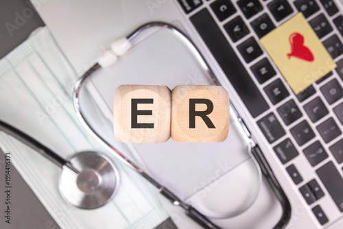 ER acronym on wooden cubes, stethoscope and heart symbol on laptop, emergency room medical concept