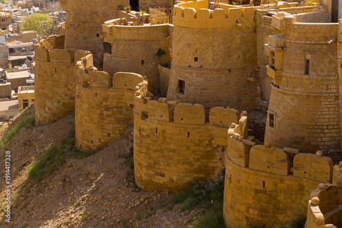 Foto Robust golden sandstone bastions form a curving defensive wall at Jaisalmer Fort, illuminated by warm sunlight and overlooking the city below