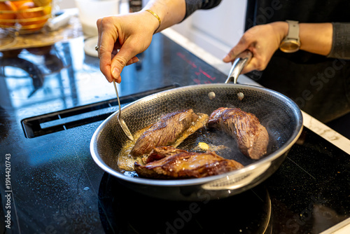 Fotografía Woman cooking beef steak in pan and basting with butter in modern kitchen