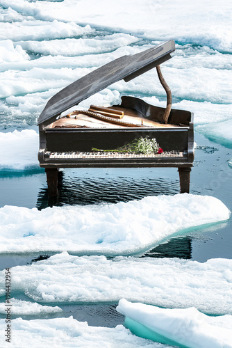 Old weathered grand piano outside in winter in water with ice flows.