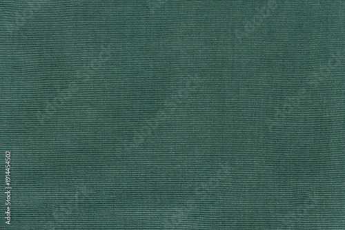 Detailed texture of a corduroy fabric in a rich green, forest, emerald tone. Top view of a ribbed velvet material background with copy space