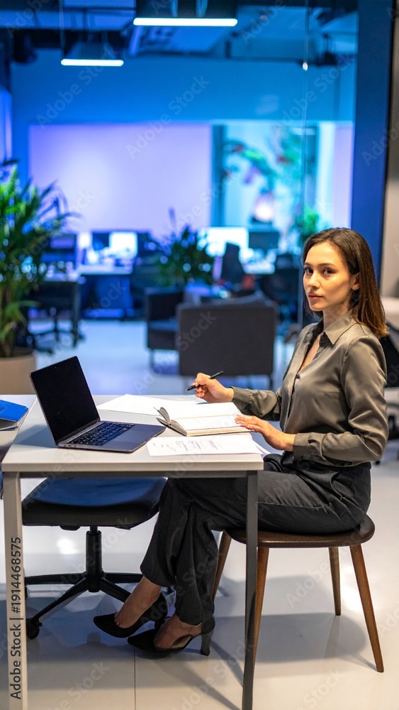 Fototapeta premium Focused young woman working on laptop in modern office, deep in thought and concentration.