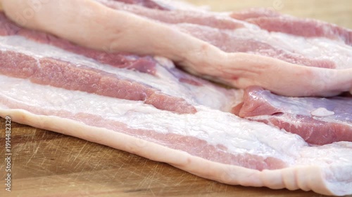 Close up fresh raw pork belly slices on wooden cutting board, uncooked meat texture and fat layers for cooking preparation, ingredient for frying, roasting, or homemade meals