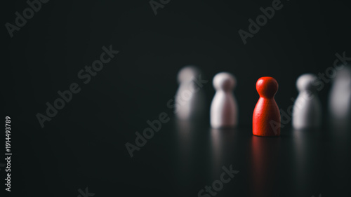 Red wooden pawn standing out from blurred white figures in dark background symbolizing leadership bold decision making individuality and strategic vision