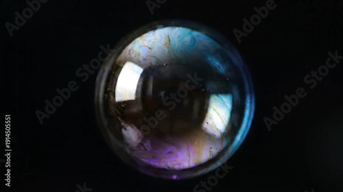 A reflective glass sphere with iridescent colors against a dark background.