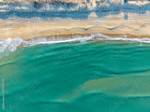 Foto Kill Devil Hills, North Carolina, a top-down aerial view of turquoise Atlantic waters crashing against a sandy beach shoreline with tire tracks on the Outer Banks