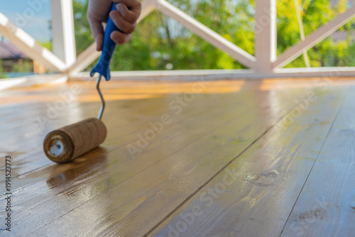 Hand painting wooden floor on sunny porch with blue handled roller